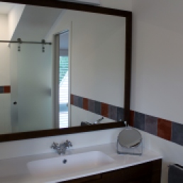 Aqui es veu el moble del bany i a traves del mirall la mampara de vidre a l'àcid tancament wc.